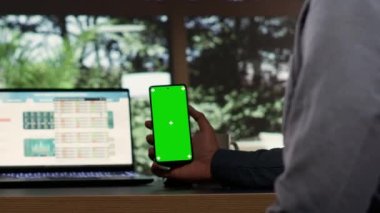 Erkek milyarder zengin dağlık evinde, zengin girişimci masasında yeşil ekran telefon ekranı kullanıyor. Genç hissedar izole edilmiş kromakeyle çalışıyor, sermaye fonlarına yatırım yapıyor..