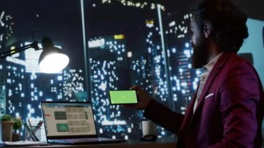 İşyeri sahibi akıllı telefon ekranında yeşil ekran kullanıyor, gökdelendeki lüks masasında oturuyor ve şirket geliştirme üzerinde çalışıyor. Finans uzmanı boş kromakey modeline bakıyor.