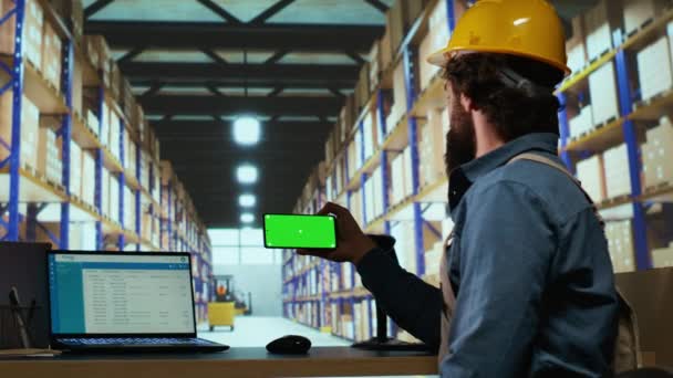 倉庫マネージャーは スマートフォンディスプレイのグリーンスクリーンを見て 産業用デポの小包の出荷と配達に取り組んでいます 空白コピースペースモックアップ画面を使用した品質管理アドバイザー — ストック動画