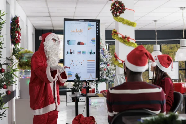 认证讲师装扮成圣诞老人 在节日华丽的工作空间教员工重要的商业成长小窍门 公众演说家向员工展示假日期间的统计图 — 图库照片
