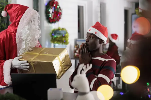 非裔美国人员工惊讶地看到同事们在寒假期间以圣诞老人的身份赠送的圣诞礼物 在节日装饰办公室给同事送圣诞礼物的工人 — 图库照片