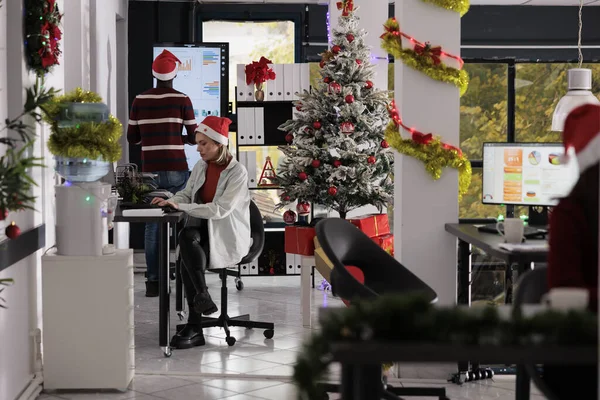 Business team working in busy festive decorated office during Christmas holiday season. Hardworking employees solving various company project tasks in xmas ornate workspace