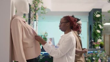 SH giyim mağazasında çalışan Afrikalı Amerikalı bir işçi müşterileri cezbetmek için şık bir spor ceket ayarlıyor. İndirimli moda mağazasında perakende satış görevlisi resmi kıyafet düğmelerini kapatıyor