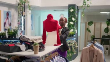 Lüks moda butiğinde çalışan titiz perakende asistanı, mankenin üzerine kadın bluzu giyiyor. Deneyimli Afro-Amerikan çalışanı yeni moda giysiler koleksiyonunu sergiliyor.