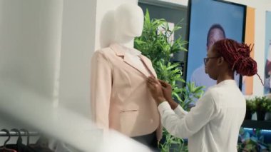İkinci el giyim mağazasında çalışan bir kadın müşterileri cezbetmek için şık bir spor ceket ayarlıyor. Mağaza görevlisi indirimli moda mağazasında resmi kıyafetlerin düğmelerini kapatıyor