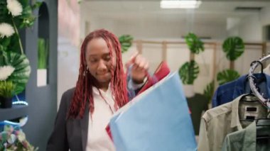 Ucuz giysiler bulduktan sonra müşterilerin mağazada dans edişlerini gösteren bir fotoğraf. Moda mağazasındaki satışlar için heyecanlanan bir kadın, alışveriş torbaları dolusu kıyafetle ayrılıyor.