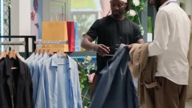 Süslü moda mağazasında, arkadaşının askı üzerinde şık kıyafetler bulmasına yardım eden bir adam. Alışverişci, en son şık tasarımcı erkek gömlekleri koleksiyonu deniyor.