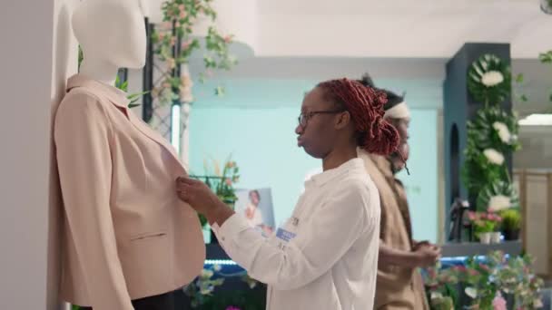 在Sh服装店工作的非洲裔美国人雇员在人体模特上穿上漂亮雅致的夹克 以吸引顾客 零售助理关闭打折时装店正式服装的纽扣 — 图库视频影像