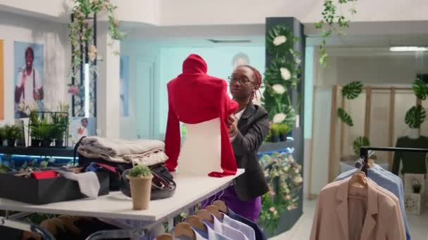 高級ファッションブティックで働く細かい小売アシスタントは 女性にマネキンにブラウスをかけます トレンディな衣服の新しいコレクションを展示する経験豊富なアフリカ系アメリカ人従業員 — ストック動画