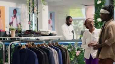 Süslü moda butiğindeki Afrikalı Amerikalı adam, çalışanlar tarafından şık ve şık kıyafetler bulunmasına yardımcı oldu. Premium showroom 'da uygun tasarımcı giysileri bulmak için müşteriye yardımcı olan yardımsever işçi