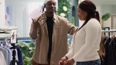 Girişimci süslü moda butiği için sosyal medya içeriğini filme alıyor, askılarda şık resmi kıyafetler sunuyor. Premium galeri sahibi yeni tasarımcı erkek koleksiyonunu tanıtıyor.