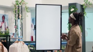 Giyim mağazasındaki BIPOC istemcisi denemek için kıyafet seçeneklerine bakmak için artırılmış gerçeklik modeli ekranı kullanıyor. Müşteri, galeride kıyafetleri görselleştirmek için kabin kullanıyor.