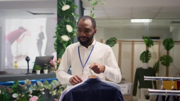 Sprzedawca Pracujący Luksusowym Butiku Mody Aranżujący Ubrania Wieszakach Afrykański Pracownik — Wideo stockowe