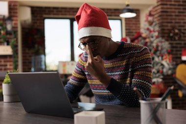 Afrika kökenli Amerikalı şirket çalışanı Noel tatili boyunca şenlikli ofiste dizüstü bilgisayarla çalışırken gözlük tamir ediyor. Noel Baba şapkası giyen genç adam son teslim tarihini yönetiyor.