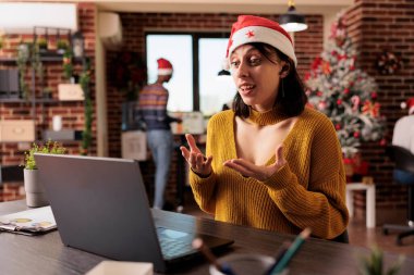 Noel Baba şapkası takan kadın video konferansında Xmas 'ı kutlamadan önce laptop kullanarak iş planlarını tartışıyor. Şirket çalışanı şenlikli işyerinde video konuşmalarıyla konuşuyor.