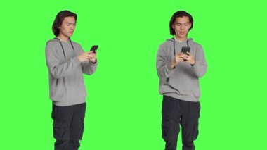 Cep telefonuna mesaj atan adam yeşil ekran arkaplanına karşı duruyor sosyal medya uygulamasını arkadaşlarıyla uzaktan sohbet etmek için kullanıyor. Asyalı neşeli yetişkin mesajları akıllı telefondan.