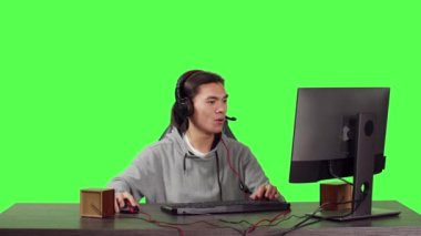 İş yerindeki erkek oyuncu bilgisayarda oynuyor, diğer insanlarla çevrimiçi video oyunları için çevrimiçi RPG turnuvası düzenliyor. Asyalı adam bilgisayarın başında tüm vücudun yeşil ekran arkaplanı üzerinde oynuyor.