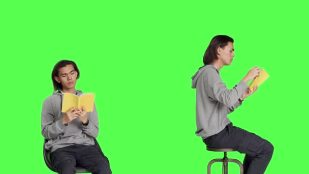 Asiatisk Kille Vilar Stol Bläddrar Litteratur Volym Mot Grön Bakgrund — Stockvideo