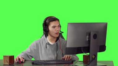 Masaüstü ofisinde oturan genç, arkadaşlarıyla eğlenirken, kulaklıklı çok oyunculu oyunların keyfini çıkarıyor. Asyalı adam yeşil ekranda rol yapma yarışmasında yarışıyor..