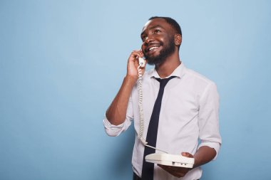 Afrika kökenli Amerikalı yetişkin bir erkek sabit hattan bir telefon görüşmesi yapıyor. Analog bir telefonda gülümseyen işadamı, sohbet ediyor. Çağdaş bir birey eğleniyor ve telefonlara bakıyor.