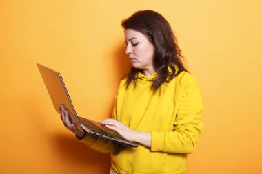 Stüdyoda elinde kablosuz bilgisayarla gezen esmer kadının portresi. Online araştırma için dijital laptopunu taşıyan ve kullanan beyaz bir kadın..
