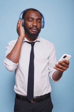 Gözleri kapalı siyah bir adamın portresi akıllı telefondan kablosuz kulaklığa kadar ses içeriğinin keyfini çıkarıyor. Genç bir ofis çalışanı, kablosuz kulaklıklardan sakinleştirici podcast dinliyor..