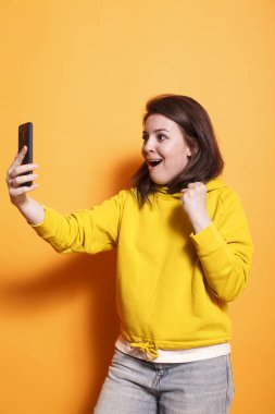 Stüdyoda mutlu bir kadın, akıllı bir telefona bakıp sırıtıyor. Heyecanlı genç bir kadın mobil cihazını tutuyor, yumruğunu sıkıyor ve zaferi kutluyor. Neşeli kadın..