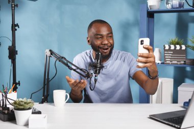 Blog yazarı akıllı telefonla içerik yaratıyor ve abonelerle konuşuyor. Gülümseyen Afro-Amerikan video kaydedicisi cep telefonuyla sosyal medya ağında canlı yayında konuşurken konuşuyor
