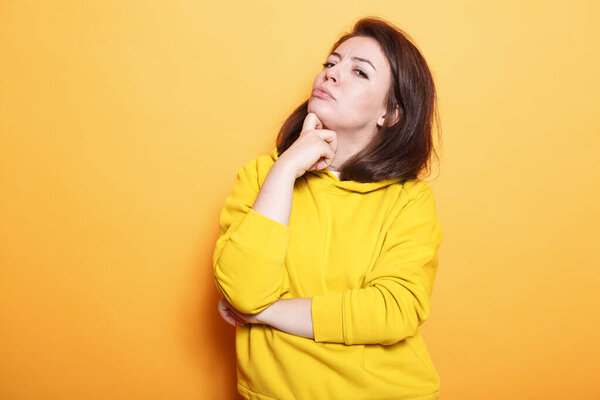 In studio, Caucasian woman thinks with her hand on her chin. Young female person is perplexed and mystified about an idea and a question. Contemplative adult with thoughtful expression.