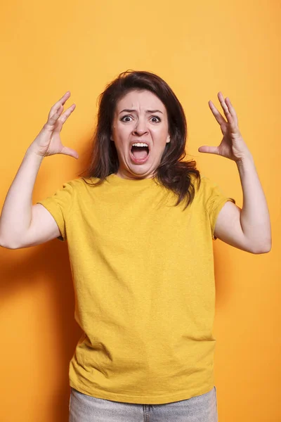 白种人女人 张开嘴 举起胳膊 传达愤怒和消极 身着休闲装的愤怒女士站在有橙色背景的工作室里 对着摄像机尖叫 — 图库照片