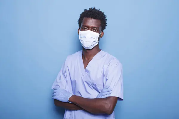 Portrait of black man wearing face mask and uniform standing in studio, working for healthcare. Medical assistant looking at camera, having protection against coronavirus.