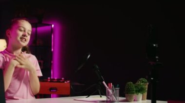 Profesyonel stüdyo olarak kullanılan pembe neon ışıklı oturma odasındaki tripodlu telefonla video çeken bir gencin görüntüsü. Genç nüfuzlu kişi, okul hakkında konuşurken cep telefonu kamerasıyla görüntüleri yakalıyor.
