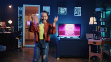 Neşeli çocuğun neon ışıklı ev stüdyosundaki inanılmaz dans figürleriyle takipçilerini büyülediği yakın çekim. Evde internet yıldızı havalı dans yetenekleri sergiliyor, aile dostu içeriği filme çekiyor.