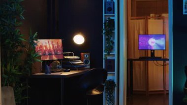 Bilgisayar ve ev bitkileriyle dolu çalışma masası. İç kısımları boş ve sıcak ışıklandırmalı. Oturma odası, güçlü PC monitörlerle çalışan 3 boyutlu animasyonlarla aydınlatılmış neon ışıklarıyla aydınlanıyor.
