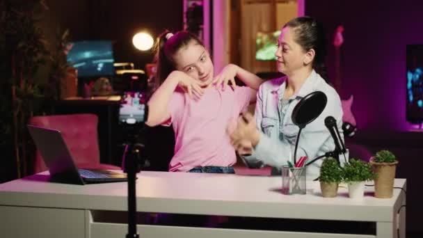若い女の子と母親はインターネットチャンネルでコンテンツを撮影し 彼らの関係について話しました バックグラウンドとしてピンクのネオン照明とアパートスタジオでキュートな子供とママのレコーディング家族Bog — ストック動画
