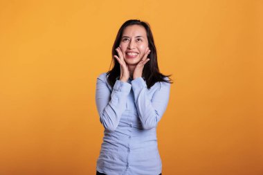 Kameranın önünde gülümseyen neşeli Filipinli kadın, sarı arka planda stüdyoda kaygısız komik ifadeler yapıyor. Neşeli model heyecanlı ve mutlu. Rahatlama zamanının tadını çıkarıyor.