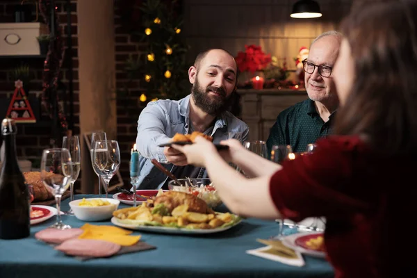 お祝いのディナーで食べ物を食べ 一緒にクリスマスを祝い 食事の皿を通り過ぎる人 自宅でホリデーのお祝いイベントを楽しんでいる人々の楽しいグループ 冬の宴 — ストック写真