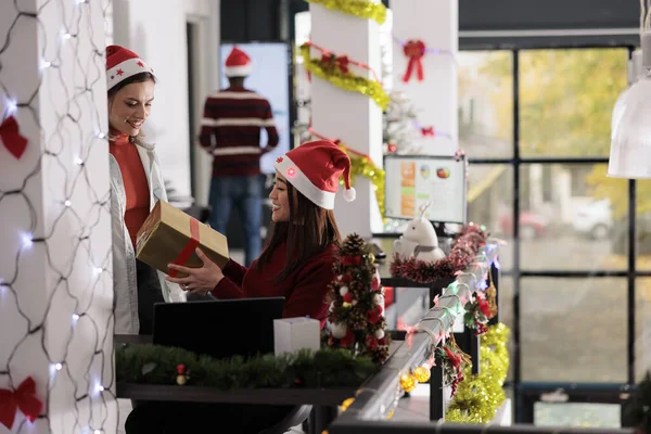 Mutlu gülümseyen Asyalı çalışan, süslü ofisteki iş arkadaşından gelen gizli Noel Baba hediyesiyle şaşırdı. Neşeli işçi kış tatili boyunca Noel hediyesi alıyor.