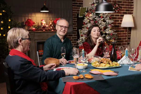 Old person at table on xmas with family eating traditional meal and celebrating christmas holiday at home. Senior people hosting festive xmas dinner event during winter season.