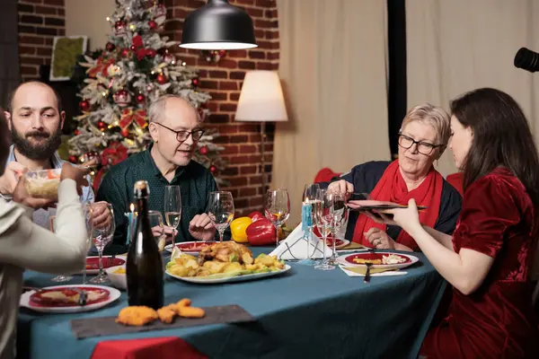 Diverse persons gathering around table to celebrate festive seasonal holiday, feeling cheerful during christmas eve dinner. Friends and family enjoying event at home with traditional homemade meal.
