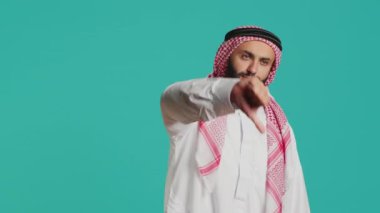 Kadim cüppeli ve kufiye giyen Müslüman adam baş parmağını kaldırıyor ve eşyalarla tatmin olmuyor. Genç kişi, stüdyo ve Arap modelinde bariz bir inkar ve olumsuz işaret gösteriyor.