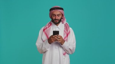 İslamcı adam mobil cihazları üzerinde çalışıyor, sosyal medya platformlarında ya da internet sayfalarında sörf yapıyor. Geleneksel kıyafetli bir Ortadoğulu Global Web 'e erişmek için akıllı telefon kullanıyor, heyecanlanıyor.