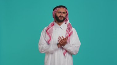 Geleneksel giysiler içinde Arap yetişkinler stüdyoda el çırpıyor, kameraya tebriklerini sunuyor ve özgüvenli bir ifadeyle tezahürat yapıyor. Müslüman adam insanları destekliyor ve alkışlıyor..