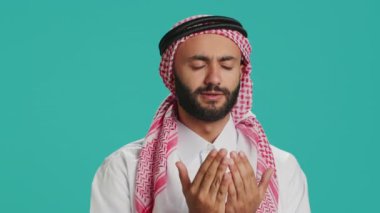 Müslüman biri kamerada Allah 'a dua ediyor, mavi arka planda dini ayinlere inanıyor. Orta Doğulu adam Tanrı 'ya meditasyonla, İslami kültürel kimlikle tapıyor..