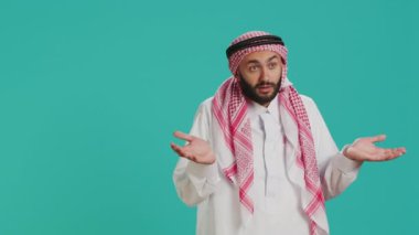 Müslüman birinin kamera karşısında kafası karışık ve kararsız olması, sembol yaratması ve mavi arka planda habersiz davranması. Arap giysili genç adam kararsız ve omuz silkiyor..
