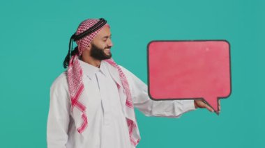 Müslüman yetişkinler konuşma baloncuklarını kameraya çekerek yeni web reklamları için reklam yaratıyor. Boş mukavva simgesi ve izole reklam tabelasıyla pazarlama sektöründe çalışan genç kişi.