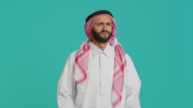 Geleneksel İslami kıyafetler giymiş Arap biri alkış işareti yapıyor, tebrik ediyor ve kendinden emin bir ifadeyle kameraya bakıyor. Müslüman adam stüdyoda destek veriyor ve alkışlıyor..