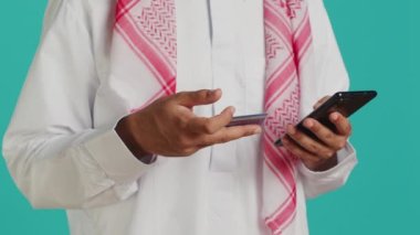 Müslüman bir adam web sitesine kart bilgileri ekliyor, geleneksel başörtüsü ile İslami kıyafetler giyerken online alışveriş yapıyor. Web mağazasında, bankacılık hizmetinde nesnelere ödeme yapan kişi