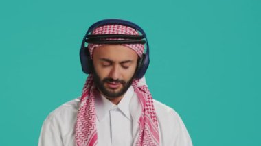 Harika bir adam kamera önünde dans ediyor, kulaklıkla modern melodileri dinliyor ve stüdyoda eğleniyor. Geleneksel kıyafetli bir Orta Doğulu dans figürleri ve şarkılar söylüyor..