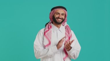 Geleneksel bornozlu Müslüman adam elleri kamerada alkışlarken gururlu bir ifade sergiliyor. Orta Doğulu beyaz tobe ve damalı ghutra giyip el çırpıyor ve tezahürat yapıyor..